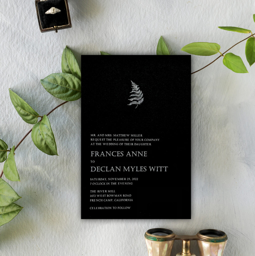 Black invitation with a fern motif and white writing.
